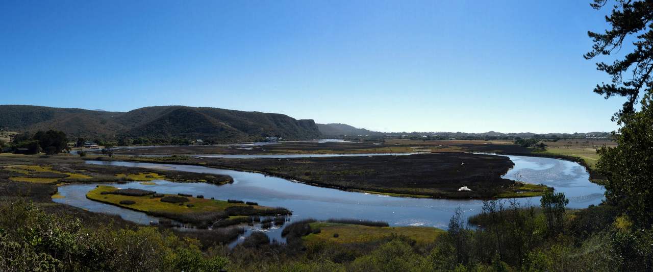 The estuary winding between reed beds, sandbanks and hills under a clear sky