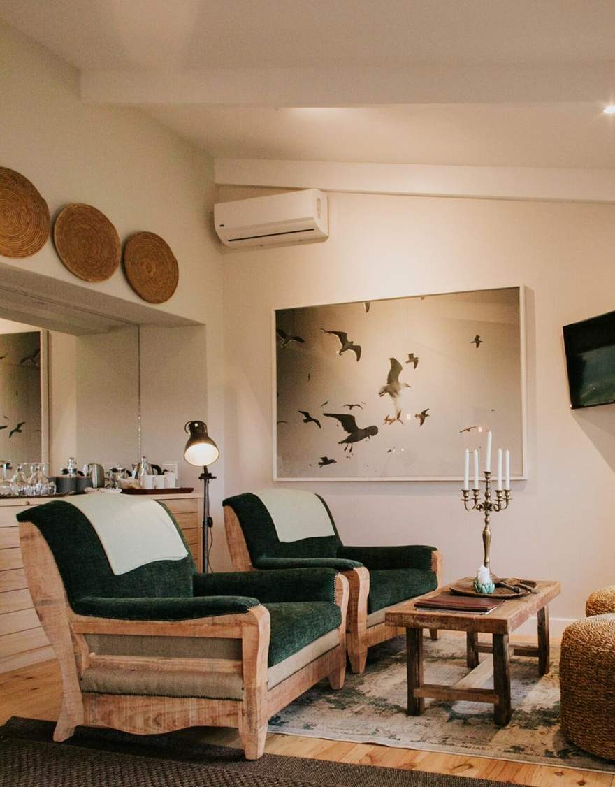 A lodge suite with green velvet armchairs, raw timber frames and a lit floor lamp