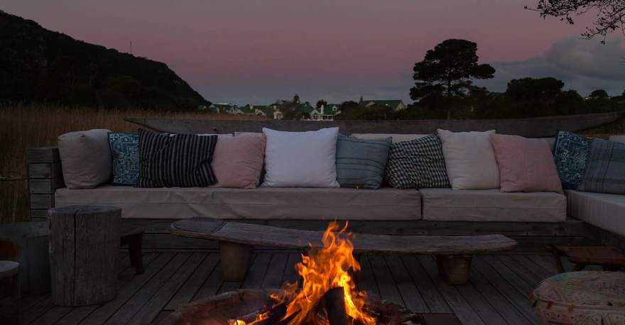 A fire burning on a deck beside cushioned benches at dusk