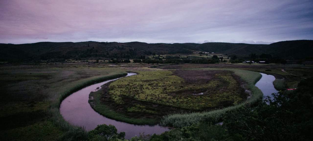 A river winding through reed beds and hills in the last light of the day
